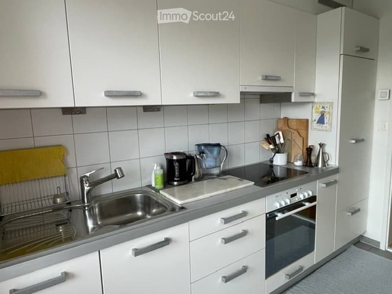 Modern kitchen with white cabinets, stainless steel sink, oven, refrigerator, and various appliances on the counter.