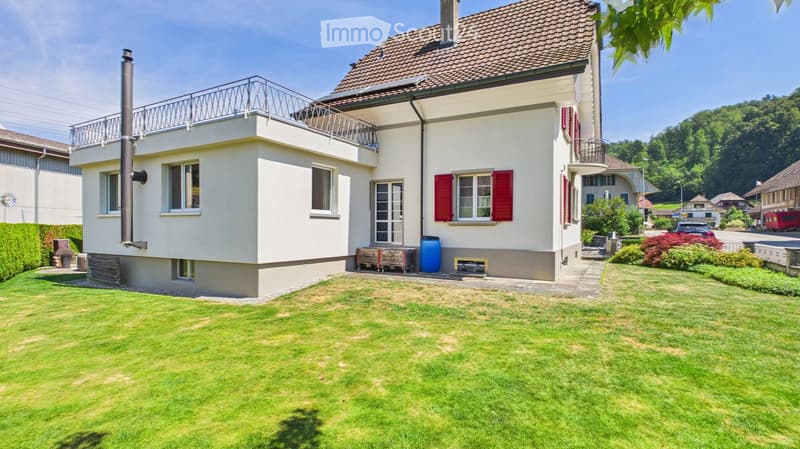 Two-story house with white walls, red shutters, and a tiled roof. Features a balcony on the upper level and a well-maintained lawn in the front yard.
