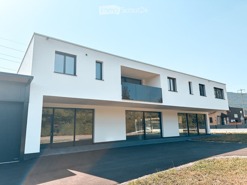 Modern two-story house with white exterior, large windows, and a balcony on the upper level.