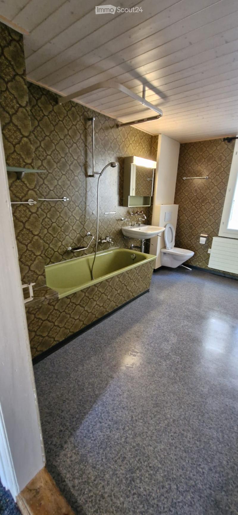 Bathroom with a green bathtub, toilet, sink, mirror, and showerhead. The walls and floor have a textured, stone-like pattern.