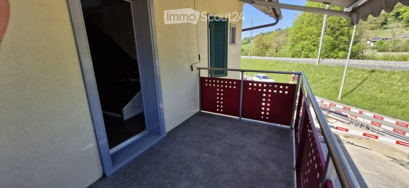 Balcony with metal railing, carpeted floor, and a view of a green landscape and road.