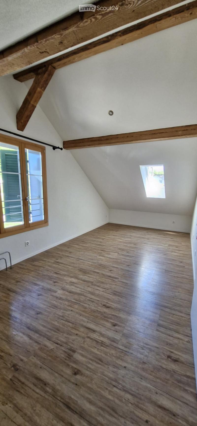 Empty attic space with wooden floors, exposed wooden beams, and skylight windows.