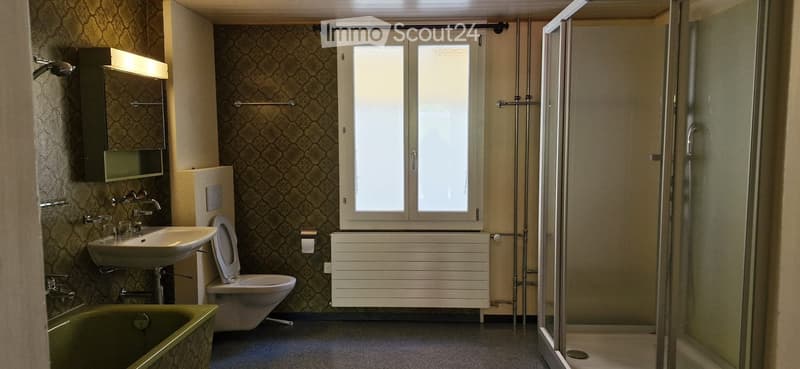 Bathroom with a sink, toilet, bathtub, mirror, radiator, and a glass-enclosed shower. The walls are patterned, and there is a window above the radiator.