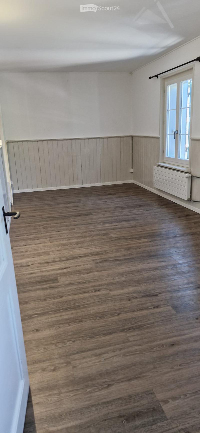 Empty room with wooden flooring, white walls, and a window with a radiator below it.