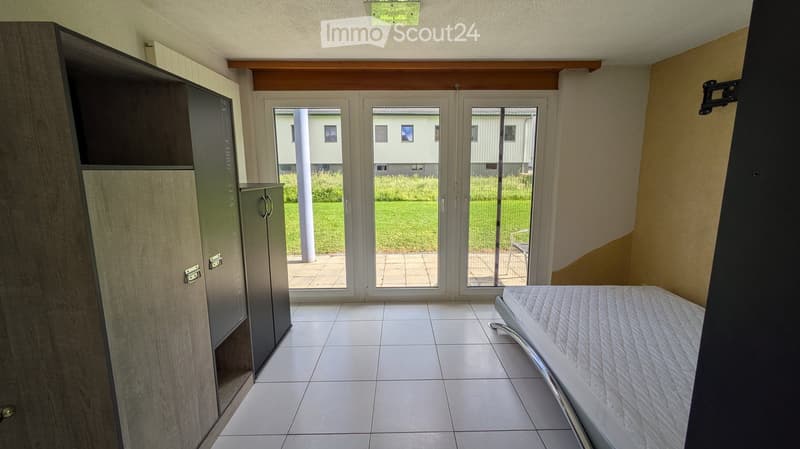 Bright bedroom with tiled floor, large sliding glass doors leading to a patio, and a built-in wardrobe.