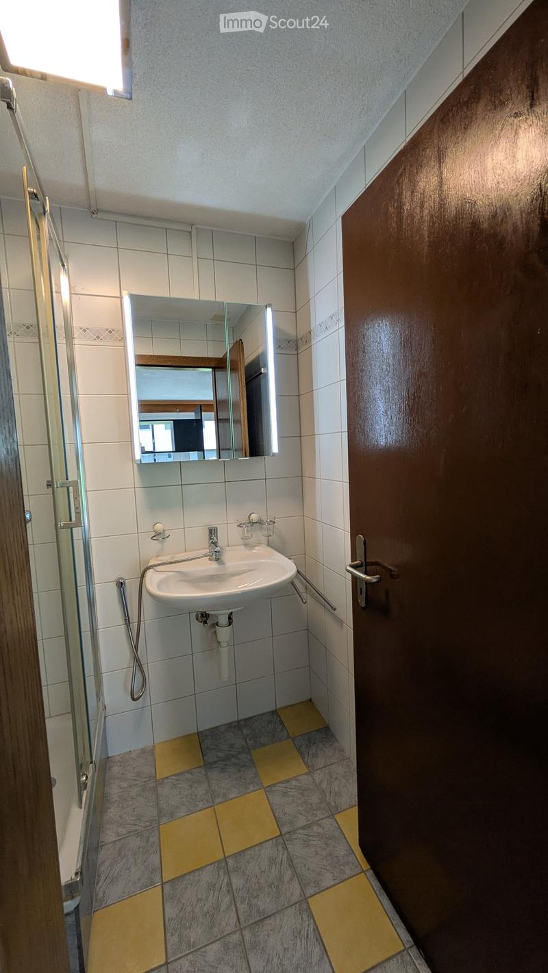 Small bathroom with a white sink, mirror, and tiled walls. The floor features a mix of gray and yellow tiles.
