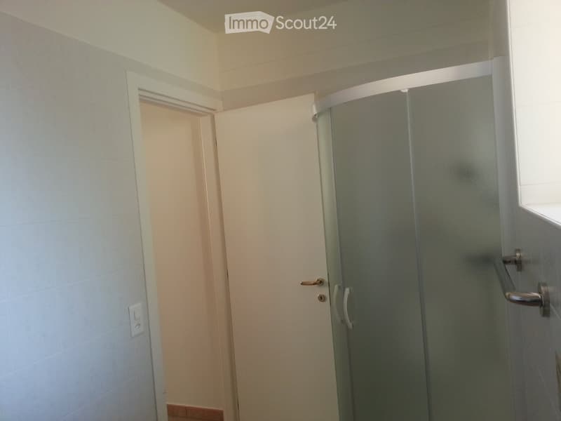 Modern bathroom with a glass-enclosed shower stall, tiled walls, and a door leading to another room.
