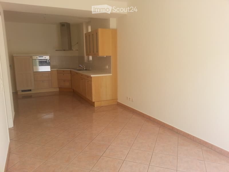 Empty kitchen with light wooden cabinets, tiled floor, and built-in appliances including an oven and sink.