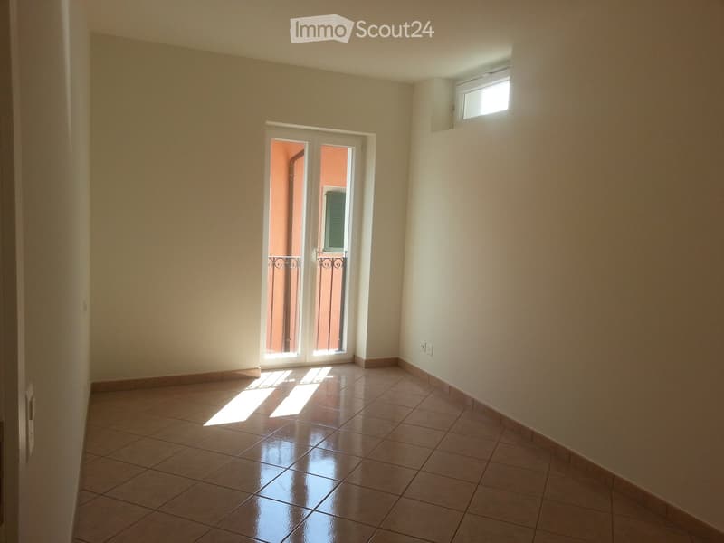 Empty room with tiled floor, white walls, and a sliding glass door leading to a balcony.