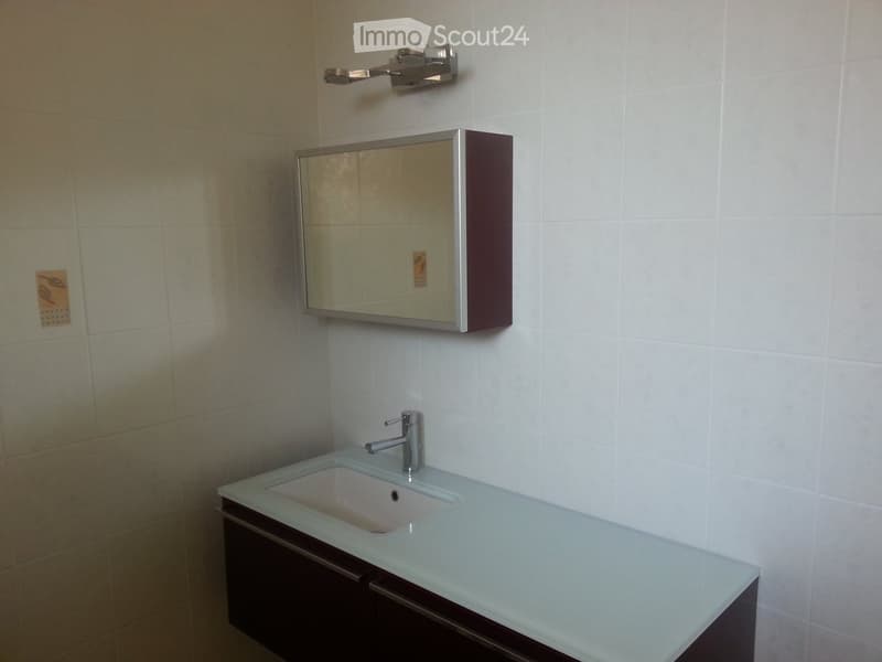Modern bathroom with a white tiled wall, a sleek sink with a chrome faucet, and a mirrored cabinet above it.