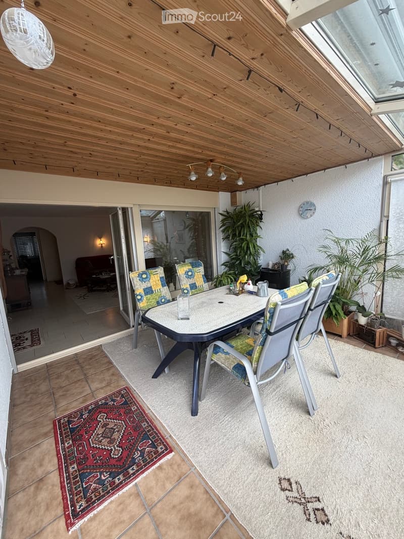 Balcony with wooden ceiling, tiled floor, table with chairs, and potted plants.
