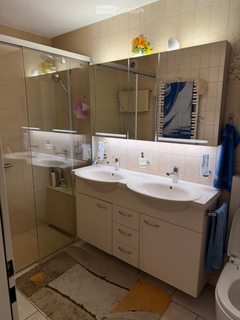 Modern bathroom with double sink, large mirror, glass-enclosed shower, and tiled walls.