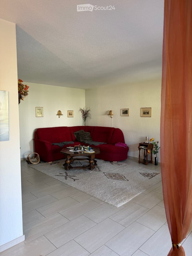 Living room with a red sectional sofa, wooden coffee table, side table, decorative vases, picture frames, and wall lamps.