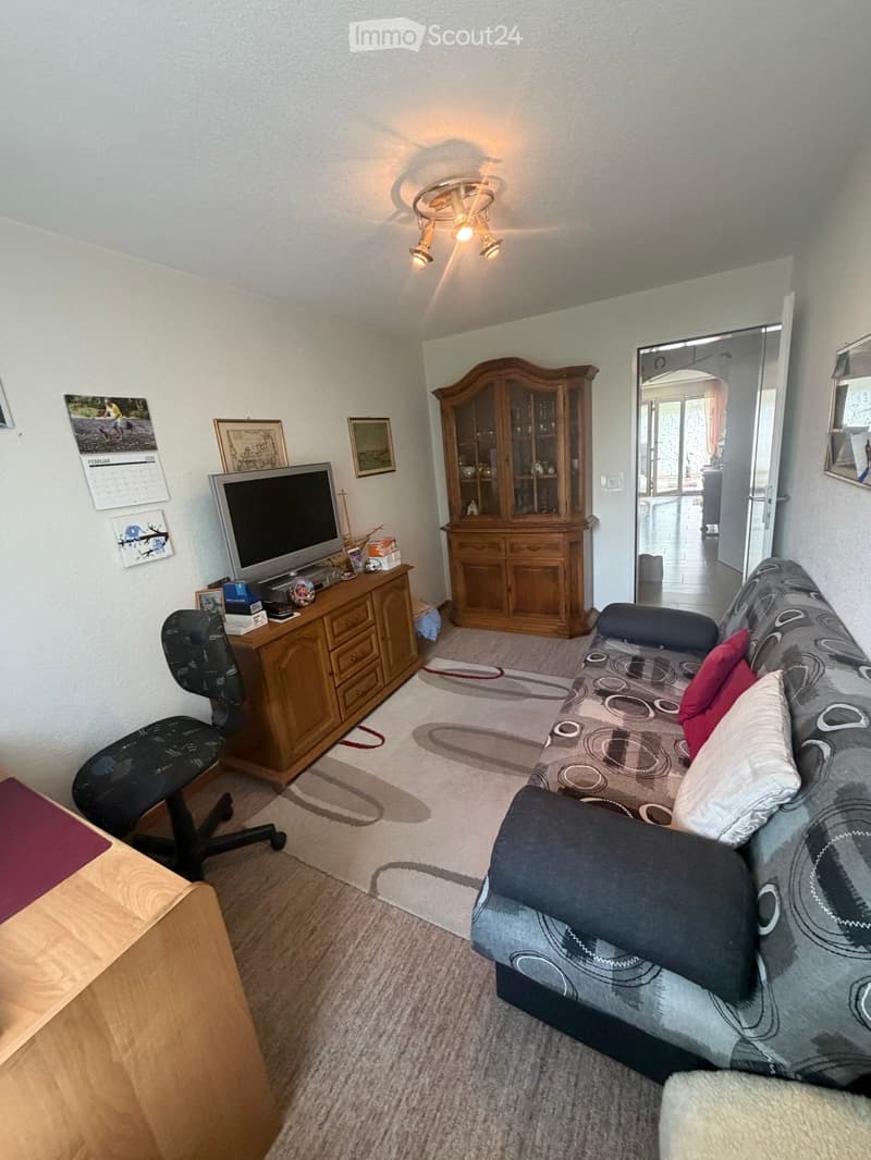 Living room with a sofa, chair, table, cabinet, television, and calendar on the wall.