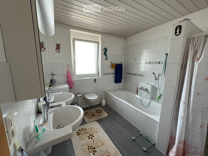 Bathroom with two sinks, a toilet, a bathtub with a shower, a mirror, and decorative towels. The room features a window and a wooden ceiling.