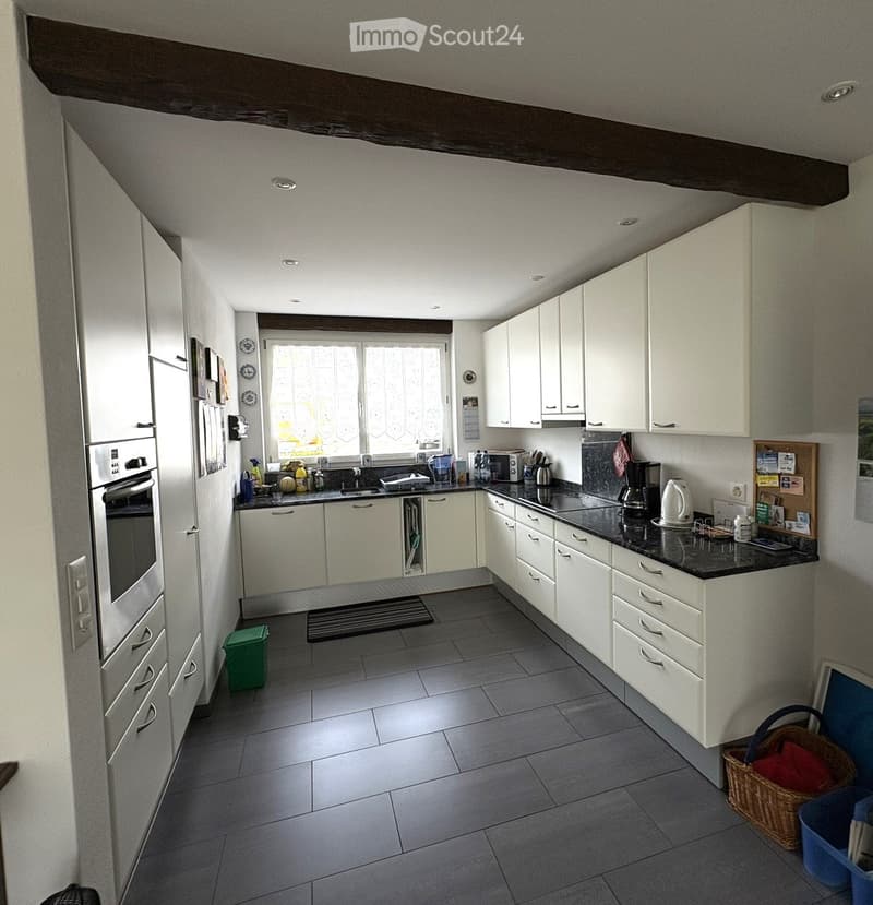 Modern kitchen with white cabinets, black countertops, and stainless steel appliances. Features include an oven, microwave, coffee maker, kettle, and various kitchen utensils on the counter.