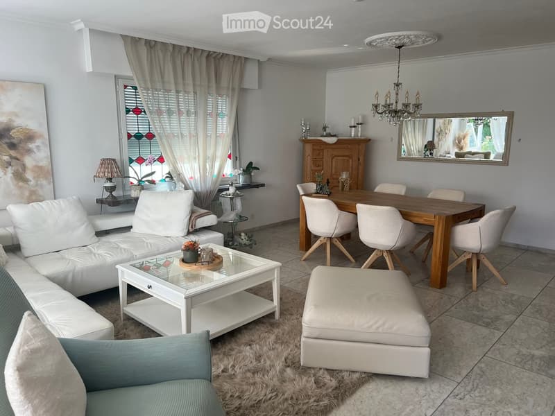Modern living and dining area with white leather sofa, glass coffee table, ottoman, dining table with chairs, chandelier, and decorative cabinet.