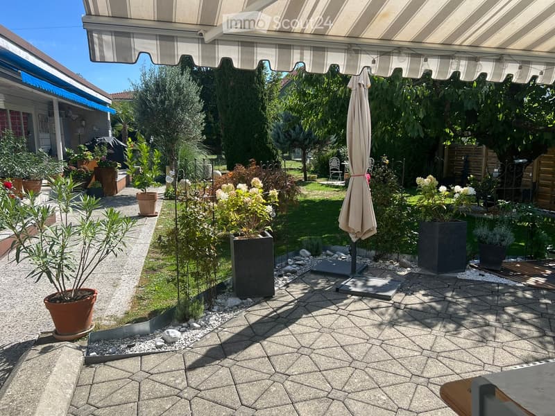 Well-maintained garden with potted plants, a patio area with a stone floor, and a covered seating area with an umbrella.