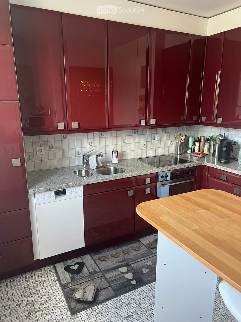 Modern kitchen with red cabinets, granite countertops, stainless steel sink, dishwasher, and oven. Includes a wooden island and various kitchen appliances.