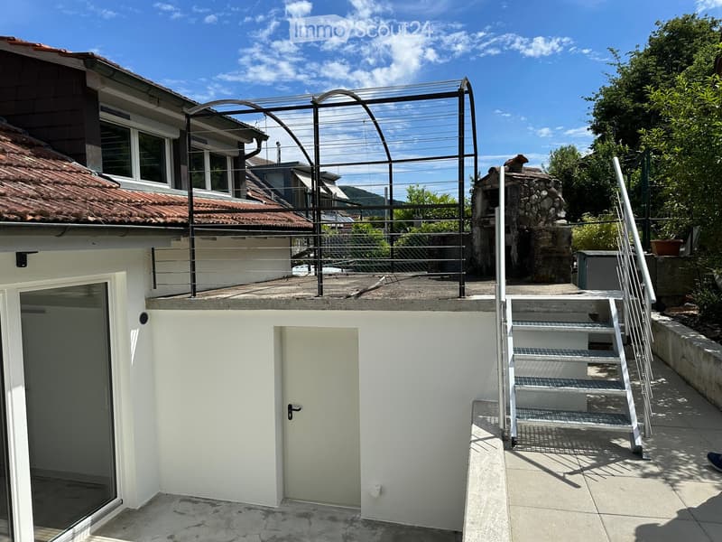 Outdoor area with a staircase leading up to a rooftop terrace, featuring a metal railing and a stone chimney structure.