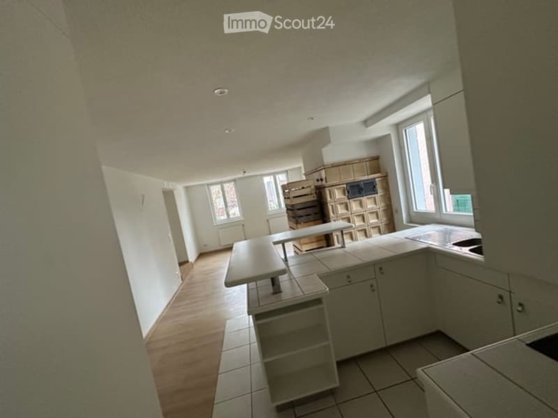 Bright, modern kitchen with white cabinets, a central island, and a dining table. The space features wooden flooring and large windows allowing natural light to fill the room.