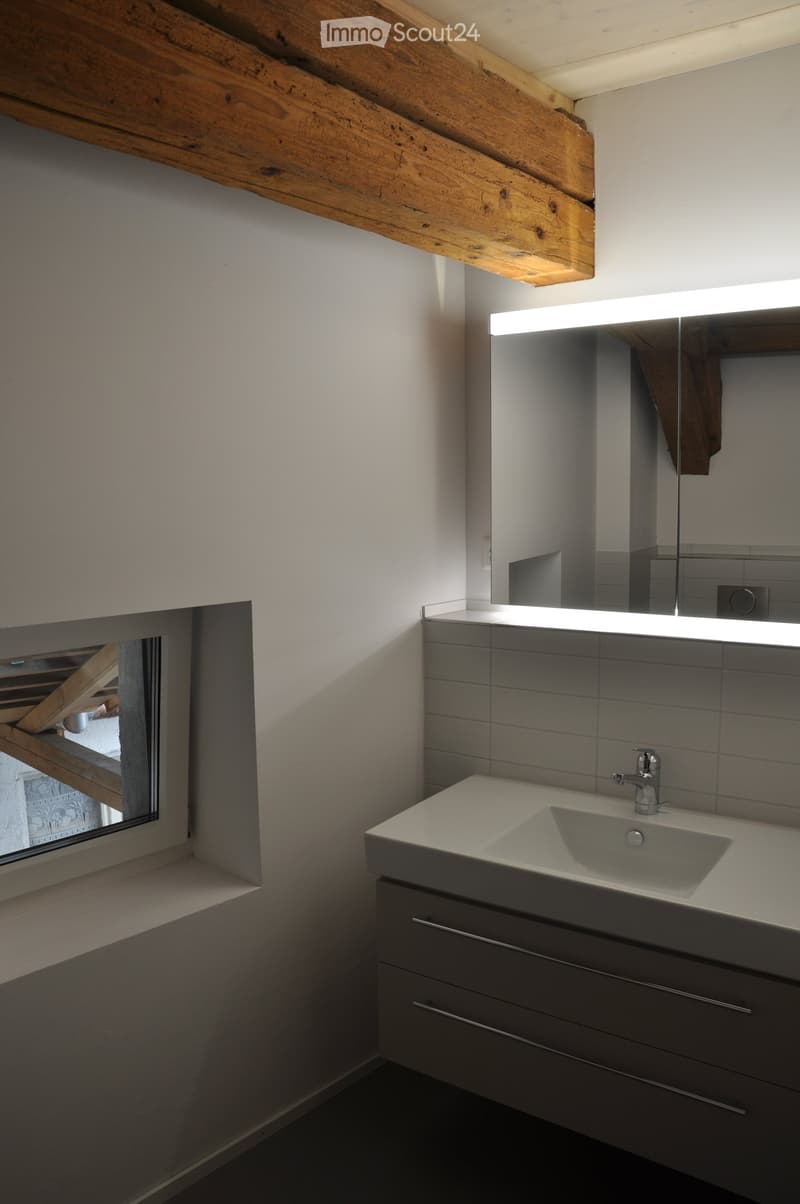 Modern bathroom with a white sink, sleek faucet, large mirror with built-in lighting, and grey cabinetry.