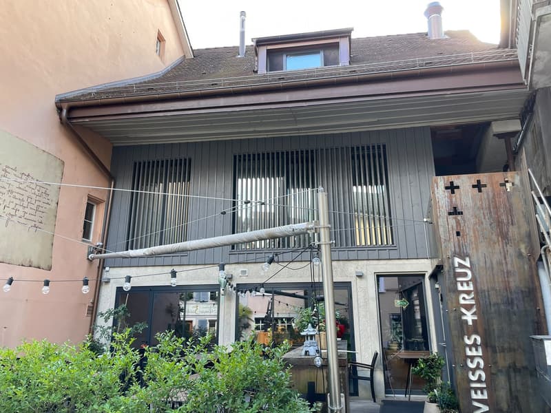 Two-story building with a modern facade, large windows, and a small outdoor seating area with tables and chairs.