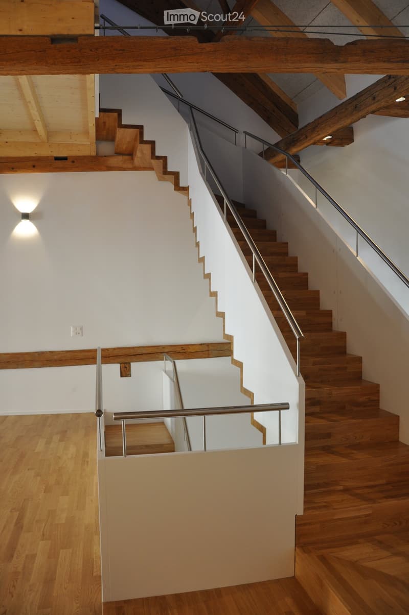 Wooden staircase with metal railing, wooden beams, and recessed lighting in a modern interior.