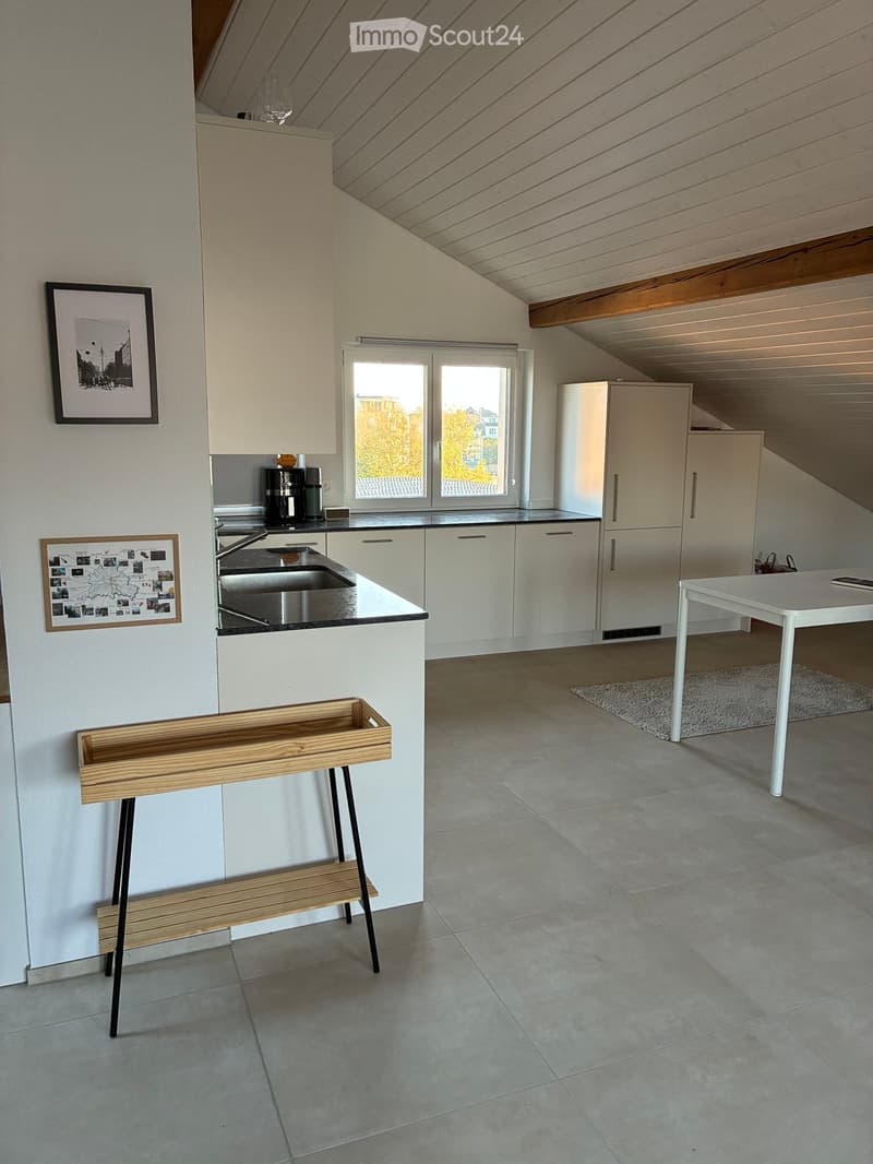 Modern kitchen with white cabinets, stainless steel sink, refrigerator, coffee maker, and a small wooden bench near the wall.