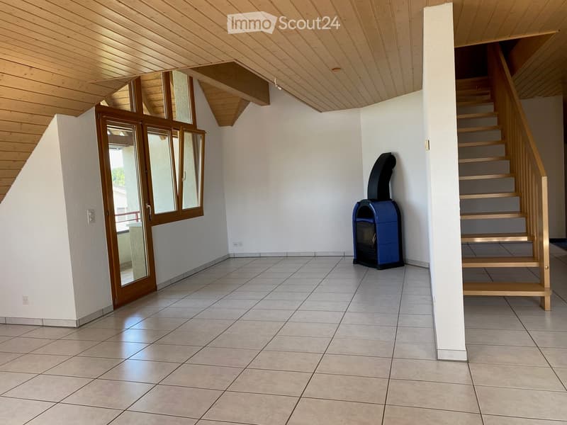 Empty room with tiled floor, white walls, wooden staircase, and a blue fireplace unit. The room has a wooden ceiling and a large window with wooden frames.