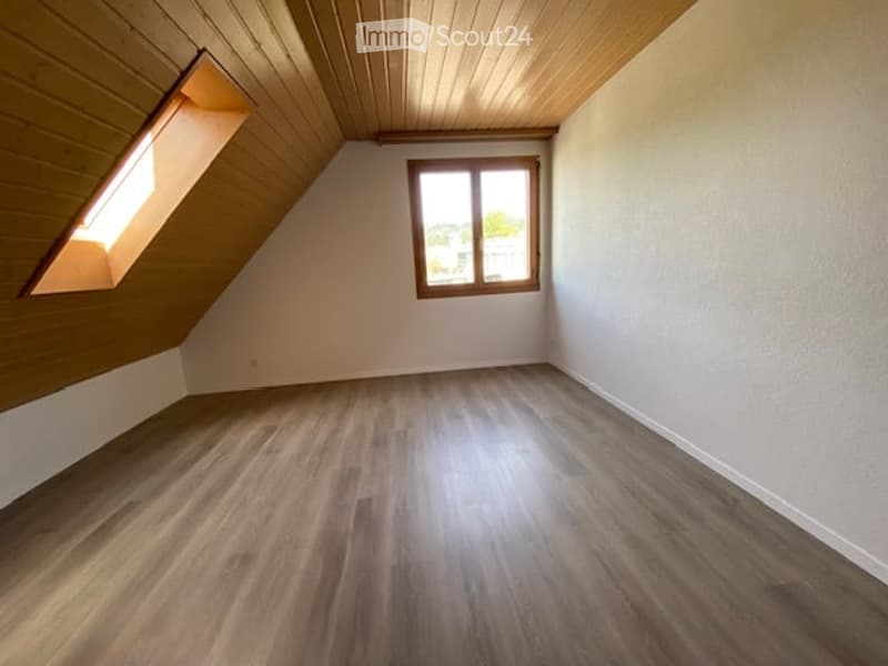 Empty attic room with wooden flooring, white walls, and two windows, one of which is a skylight.
