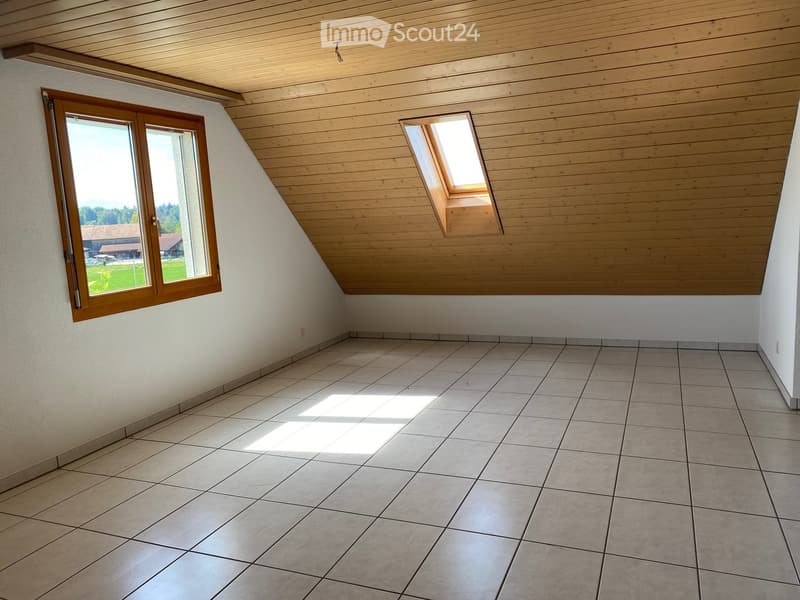 Empty room with tiled floor, wooden slanted ceiling, and two windows, one of which is a skylight. Natural light streams in, illuminating the space.