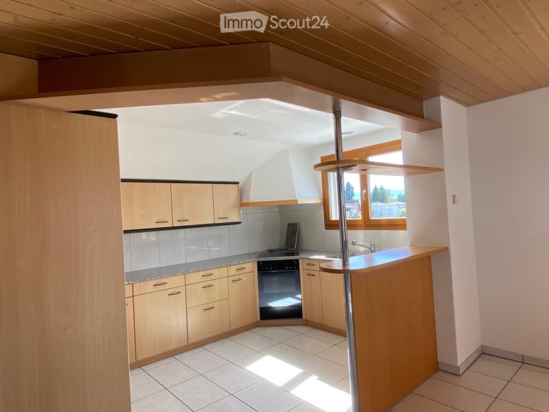 Bright kitchen with wooden cabinets, granite countertop, built-in oven, and a central island with a bar counter. Natural light streams in from a large window.