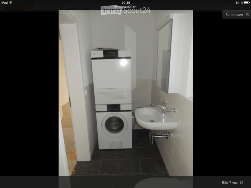 Compact bathroom with a washing machine, sink, and mirror. The space features tiled walls and a dark tiled floor.