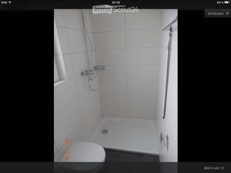 Modern bathroom with white tiled walls and floor, featuring a toilet, a shower area with a handheld showerhead, and a built-in shelf.