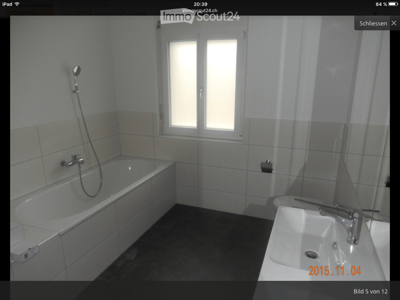 Modern bathroom with a bathtub, sink, and showerhead. The room features tiled walls and a dark tiled floor, with a window providing natural light.
