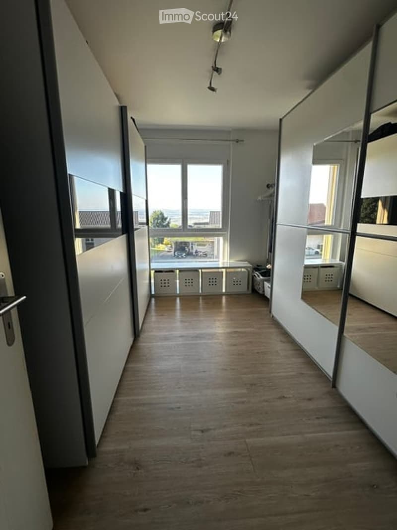 Empty hallway with wooden flooring, white walls, large windows, and built-in storage units.