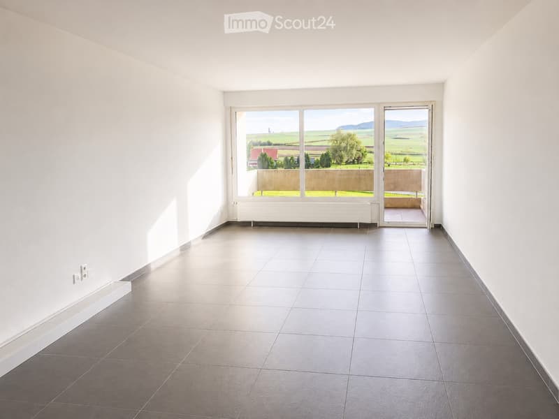 Empty room with white walls, tiled floor, large window and sliding glass door leading to a balcony with a scenic view.