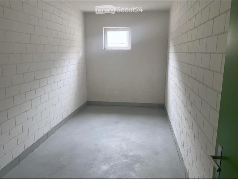 Empty room with bare brick walls, concrete floor, and a small window at the far end.