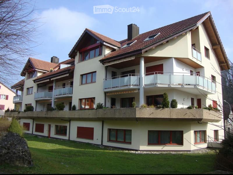 A modern two-story house with a red-tiled roof, white exterior, multiple balconies, and a well-maintained lawn.