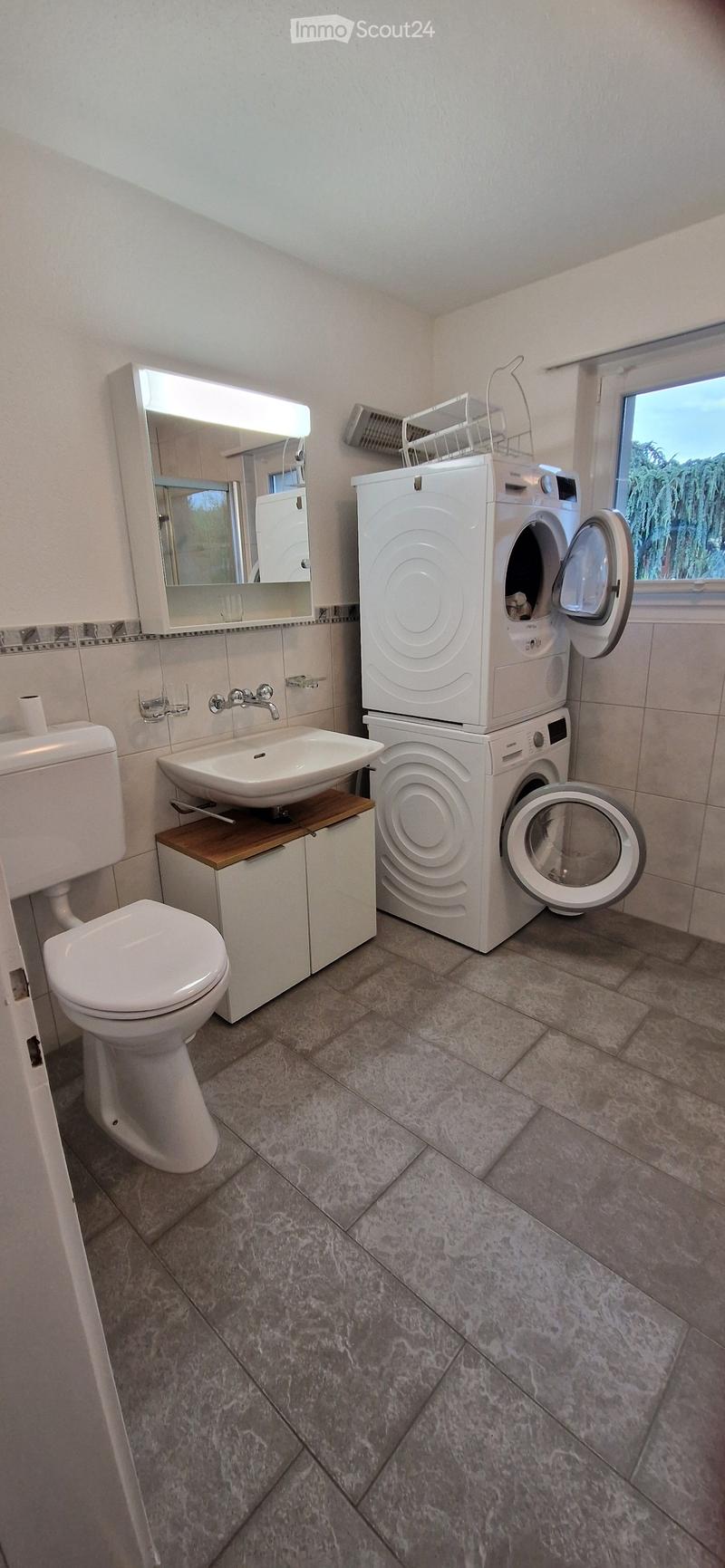 Bathroom with a toilet, sink, mirror, and stacked washing machine and dryer unit.