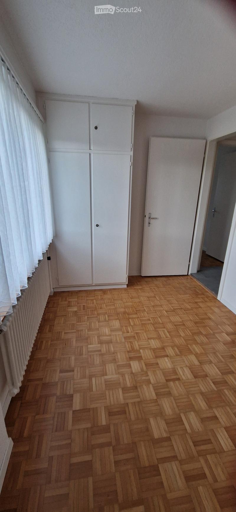 Empty room with wooden herringbone flooring, white walls, built-in white cabinets, and a white door leading to another space.