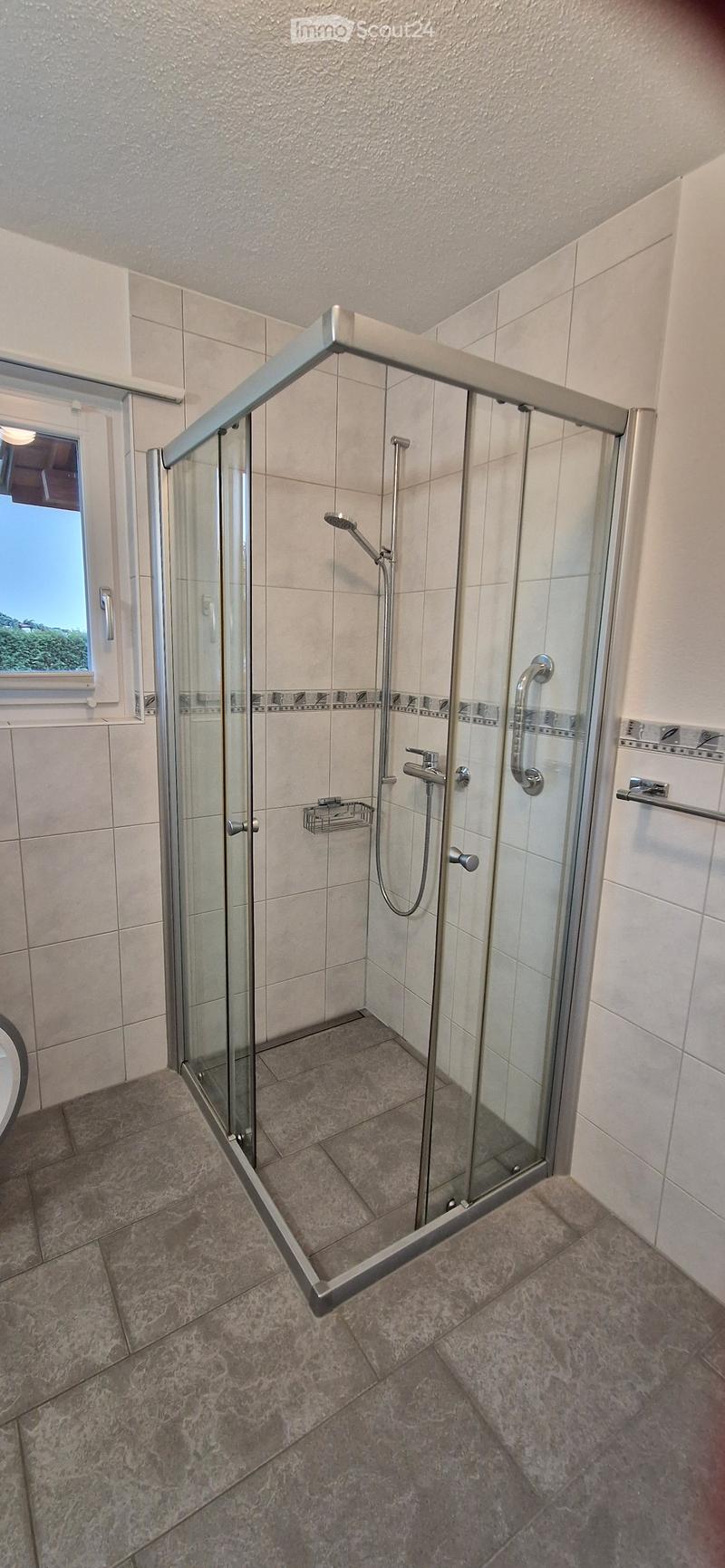 Modern bathroom with a glass-enclosed shower, tiled walls and floor, and a window providing natural light.
