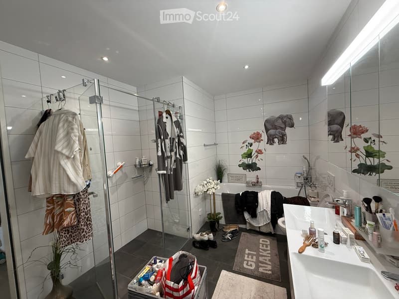 Modern bathroom with white tiles, a large mirror, a bathtub, a shower, a sink, and various toiletries. Includes decorative elements like a plant and a rug.