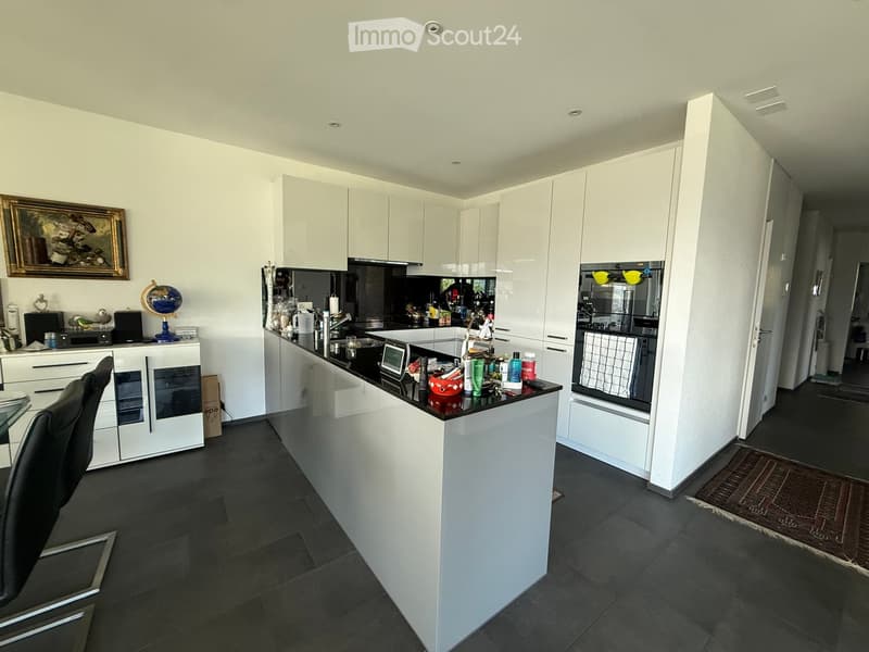 Modern kitchen with white cabinets, black countertops, and stainless steel appliances. Features a central island, sink, microwave, and various kitchen items on the counter.