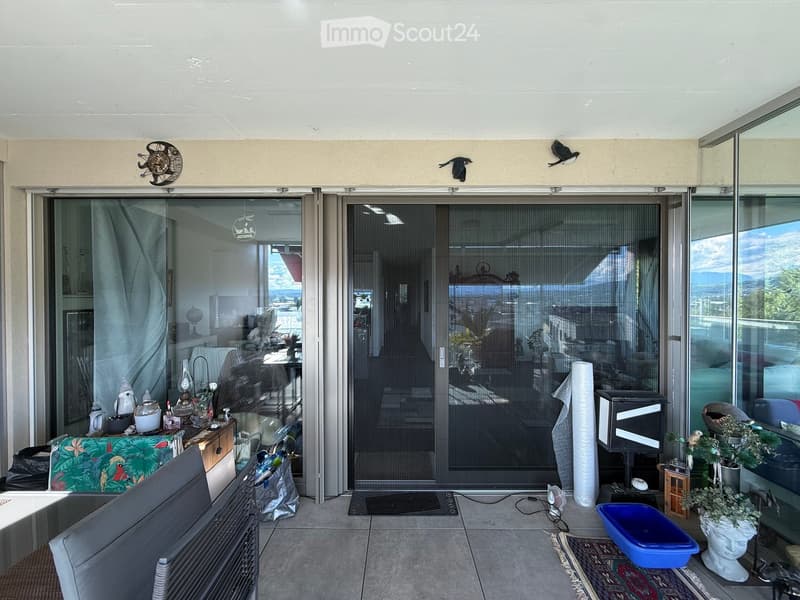 Balcony with tiled floor, large glass sliding doors, a chair, a small table with decorative items, a cat litter box, a rug, and a cat tree.