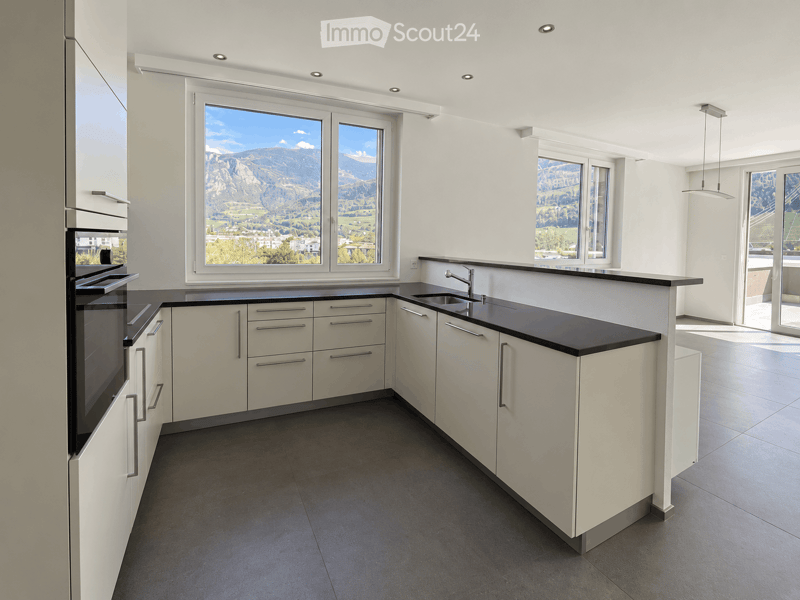 Modern kitchen with white cabinets, black countertops, stainless steel sink, and a view of mountains through large windows.