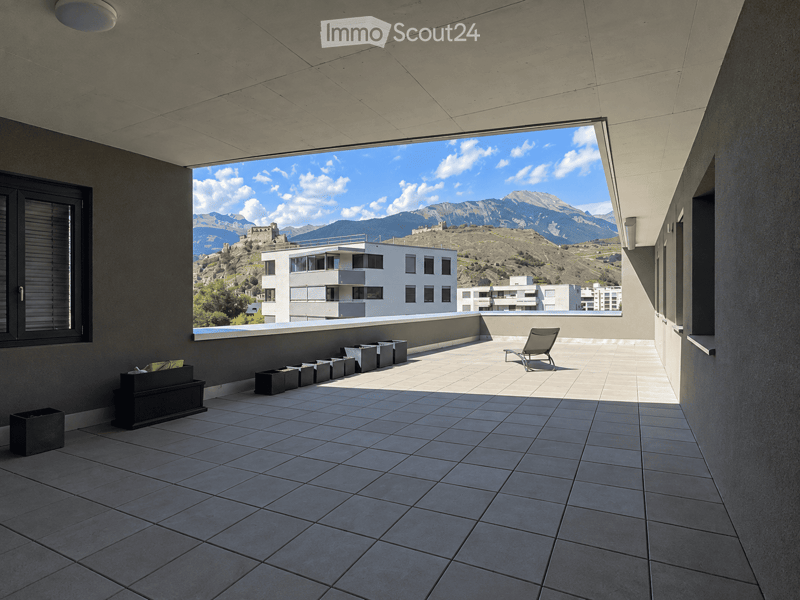 Modern balcony with tiled floor, large window offering a scenic mountain view, and a single lounge chair.