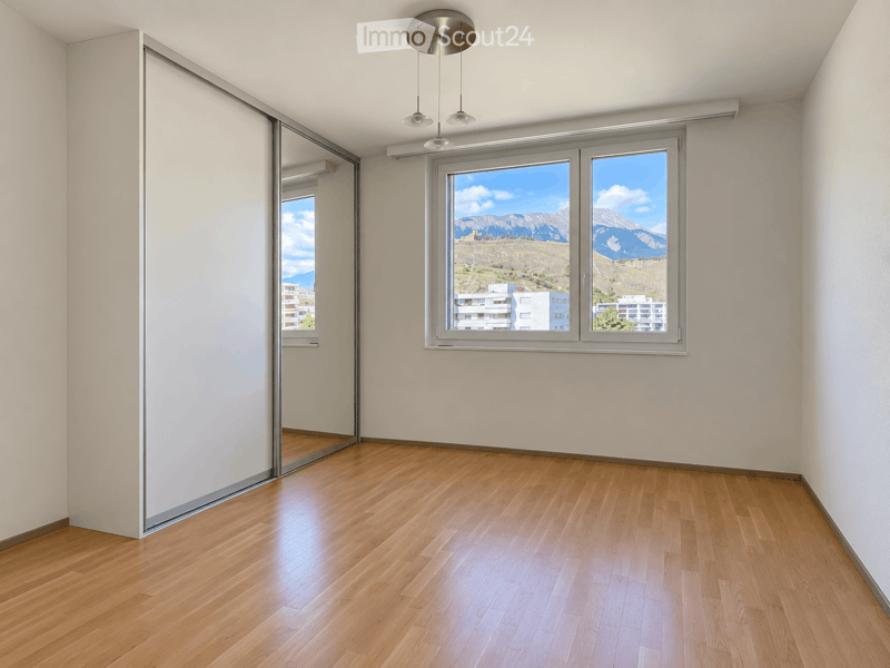 Empty room with wooden flooring, large windows offering a scenic mountain view, and modern lighting fixtures.