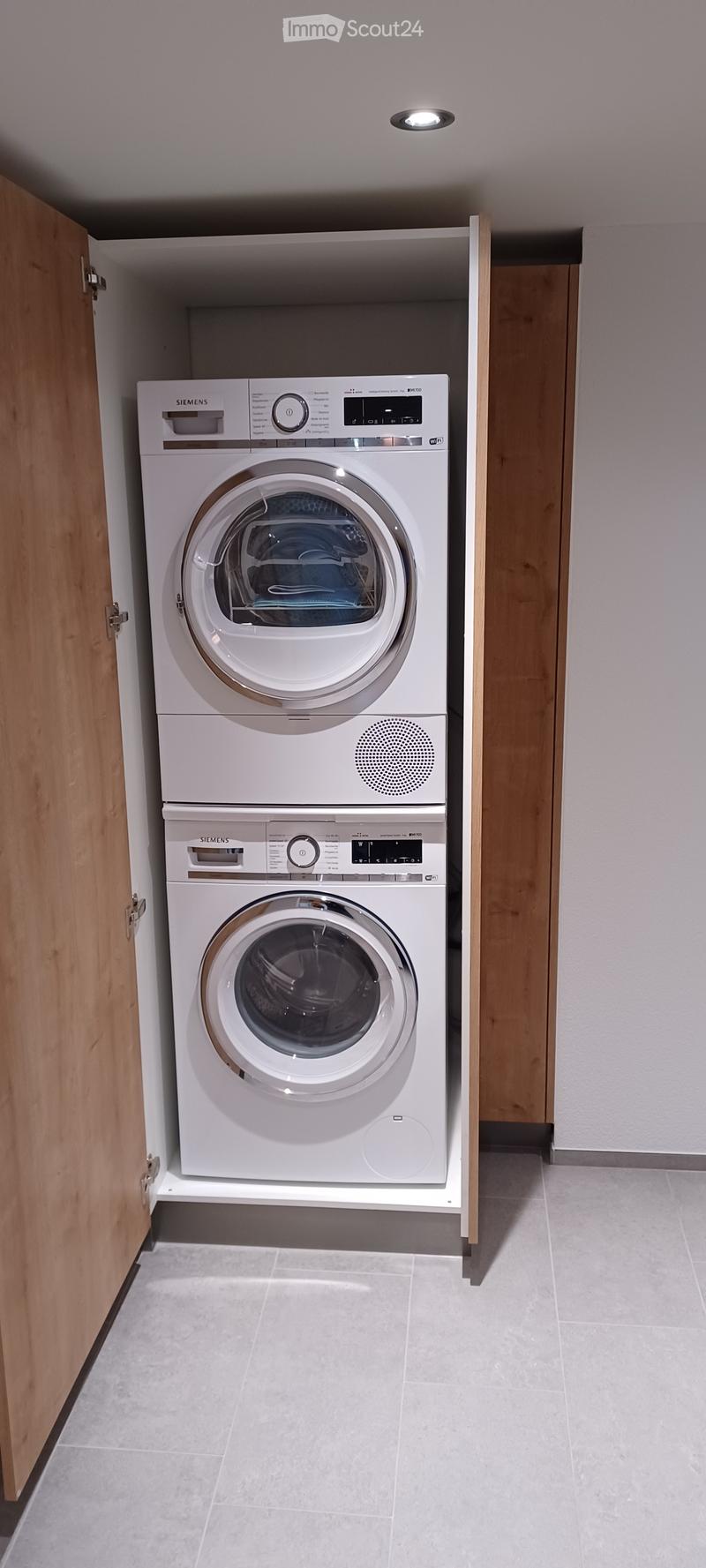 Stacked washing machine and dryer, light grey tiles, wooden doors, light recessed in ceiling